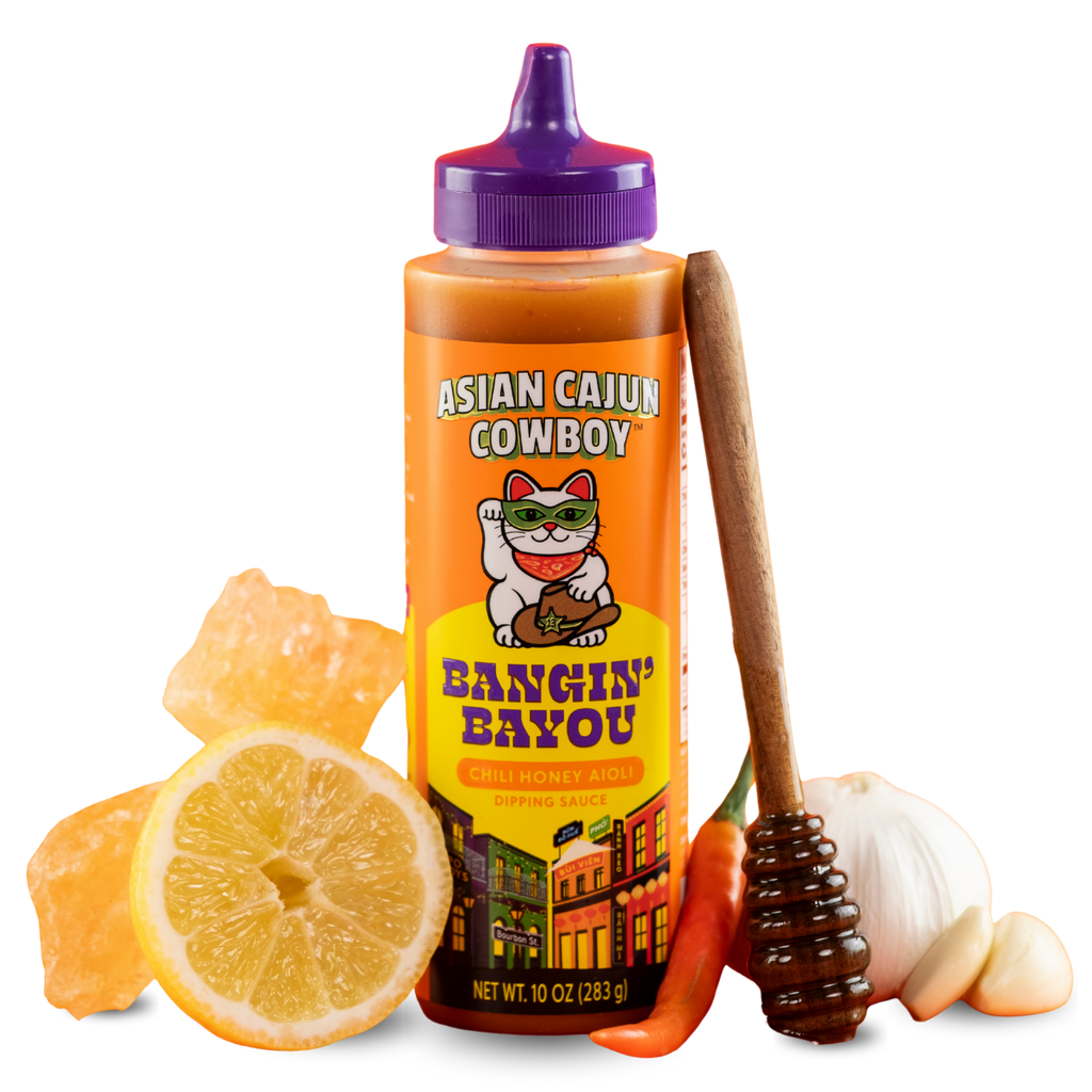 Squeeze bottle of 'Asian Cajun Cowboy' sauce with a spoon, lemon, and garlic on a white background