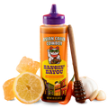 Squeeze bottle of 'Asian Cajun Cowboy' sauce with a spoon, lemon, and garlic on a white background