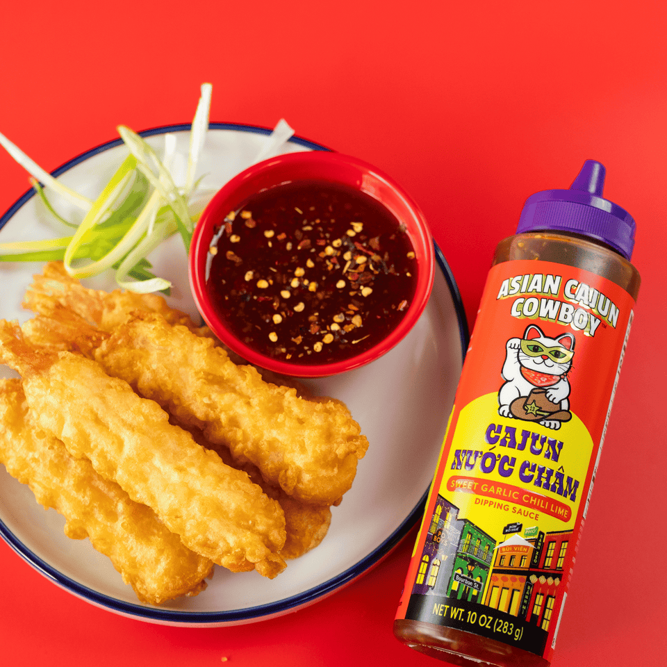 Cajun Nuoc Cham dipping sauce bottle next to fried shrimp and a bowl of sauce with a red background.