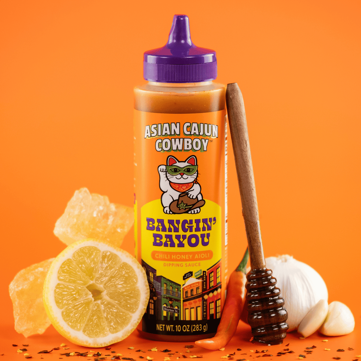 Asian Cajun Cowboy Bangin Bayou dipping sauce bottle surrounded by ingredients on an orange background.