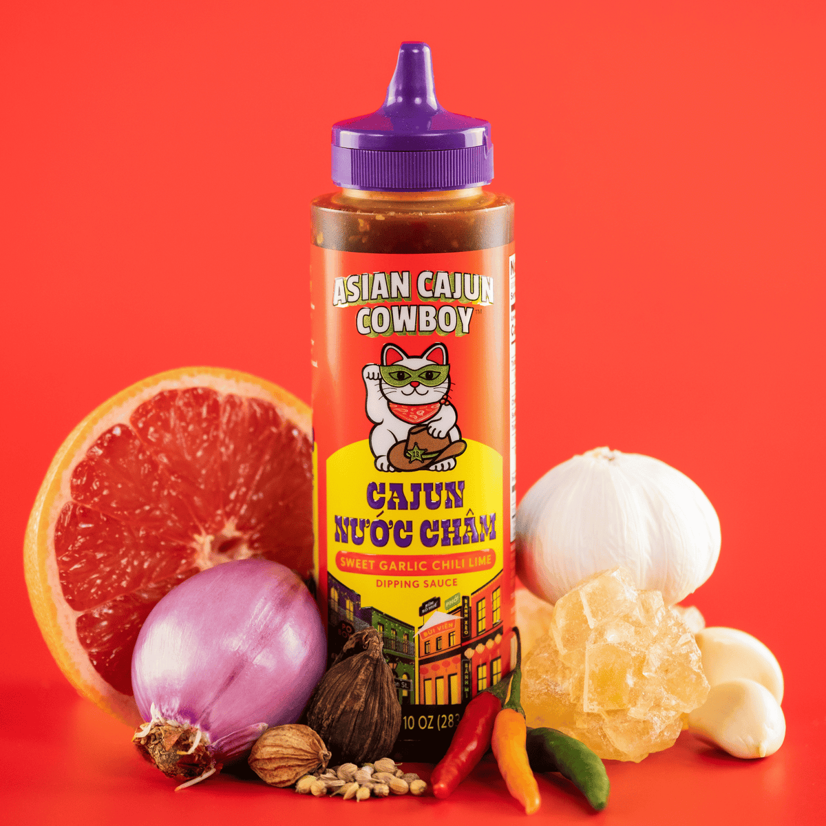 Asian Cajun Cowboy Cajun Nuoc Cham bottle surrounded by ingredients on a red background.