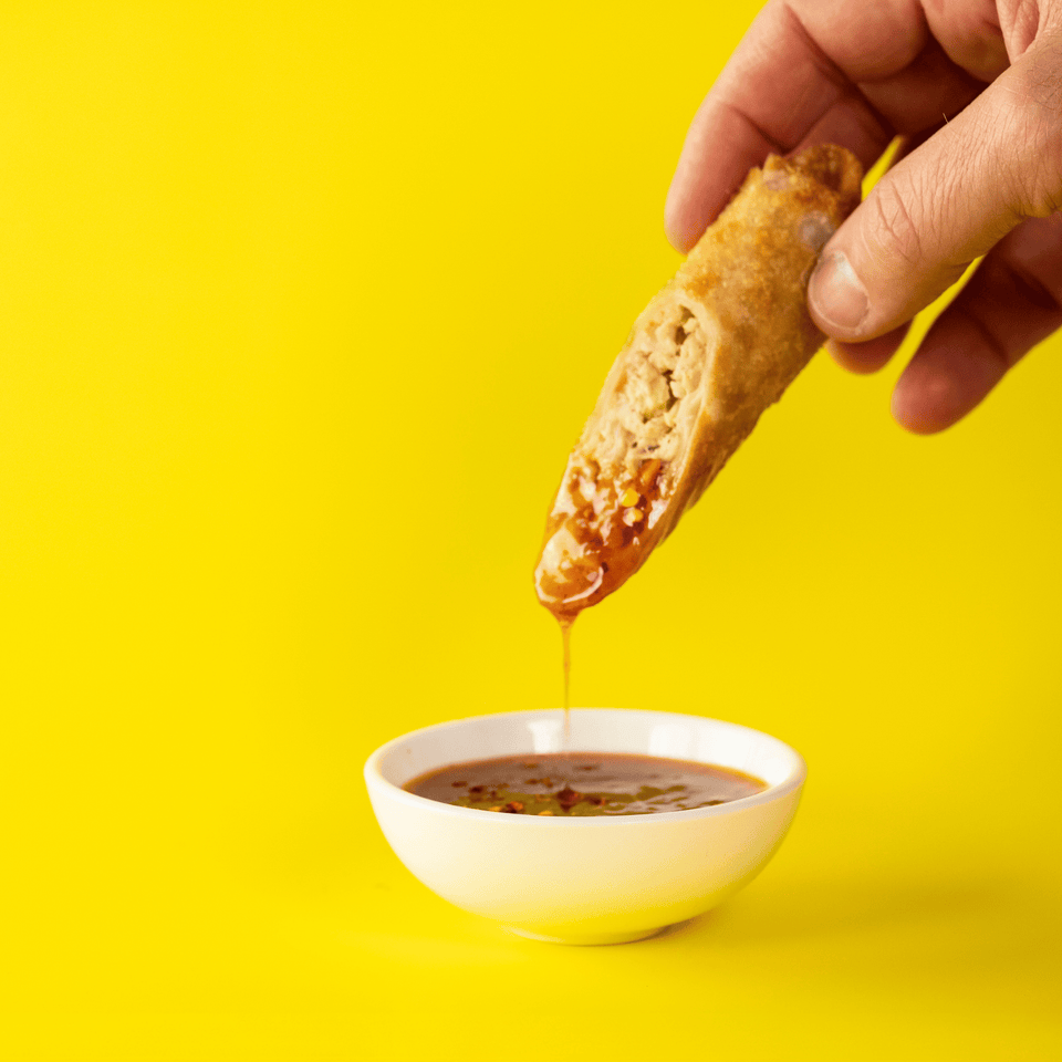 Eggroll being dipped into a sauce with a yellow background.